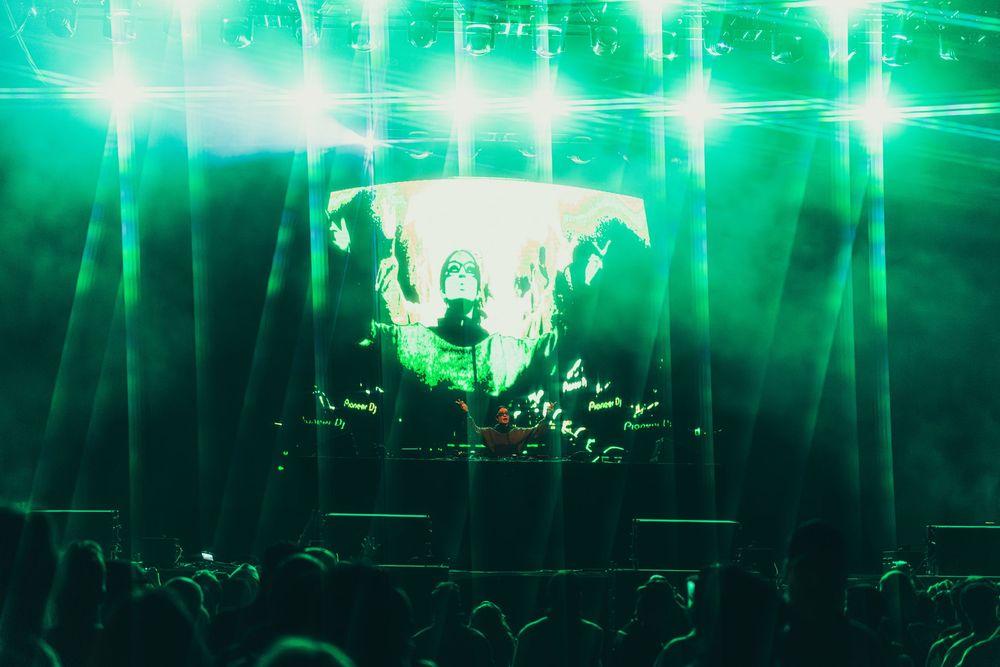 Concert venue illuminated with bright green stage lights creating an atmospheric glow over the crowd.