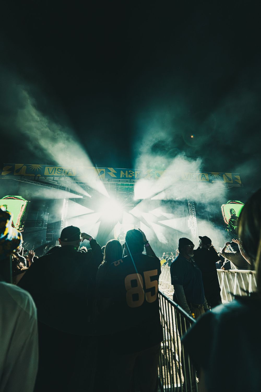 Silhouettes of fans at a nighttime sports event with bright flares and smoke creating an atmospheric scene.