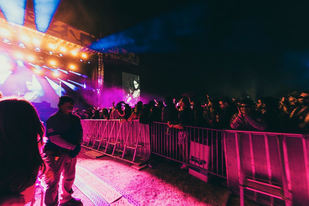 Concert crowd silhouettes against vibrant pink and blue stage lighting at a nighttime music performance.
