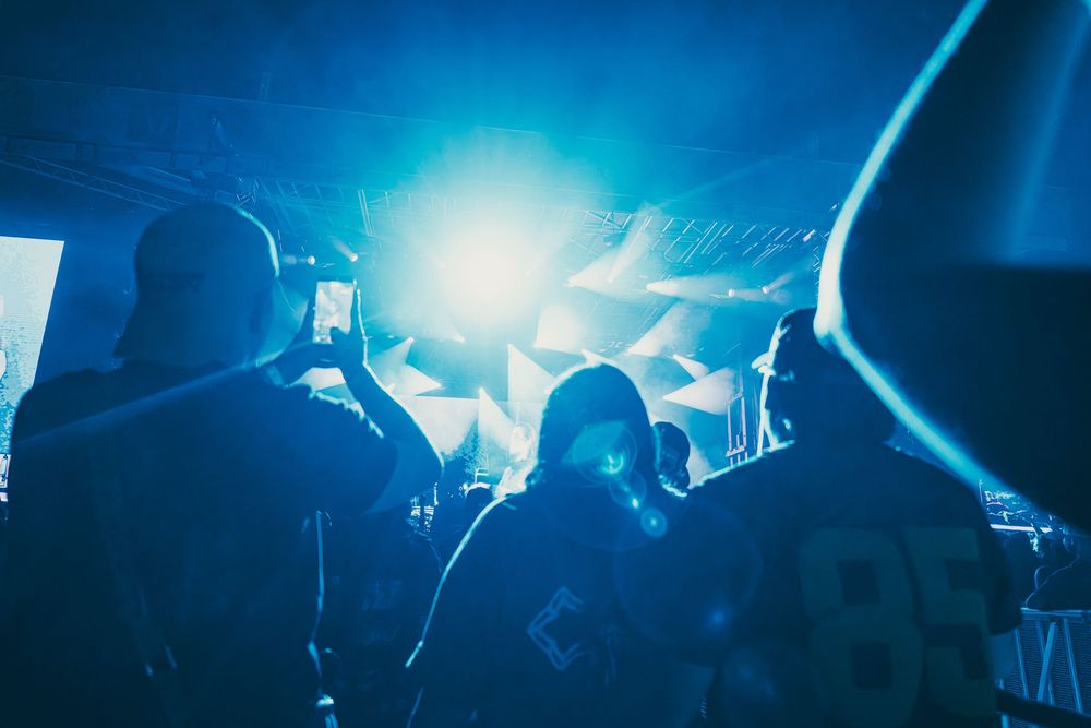 Concert crowd silhouettes against bright blue stage lights during a live music performance.
