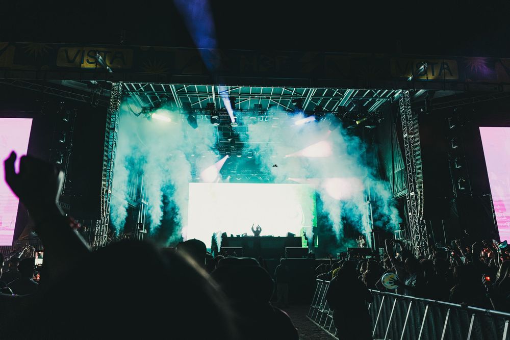 Concert crowd silhouettes against vibrant turquoise stage lighting during a live music performance.