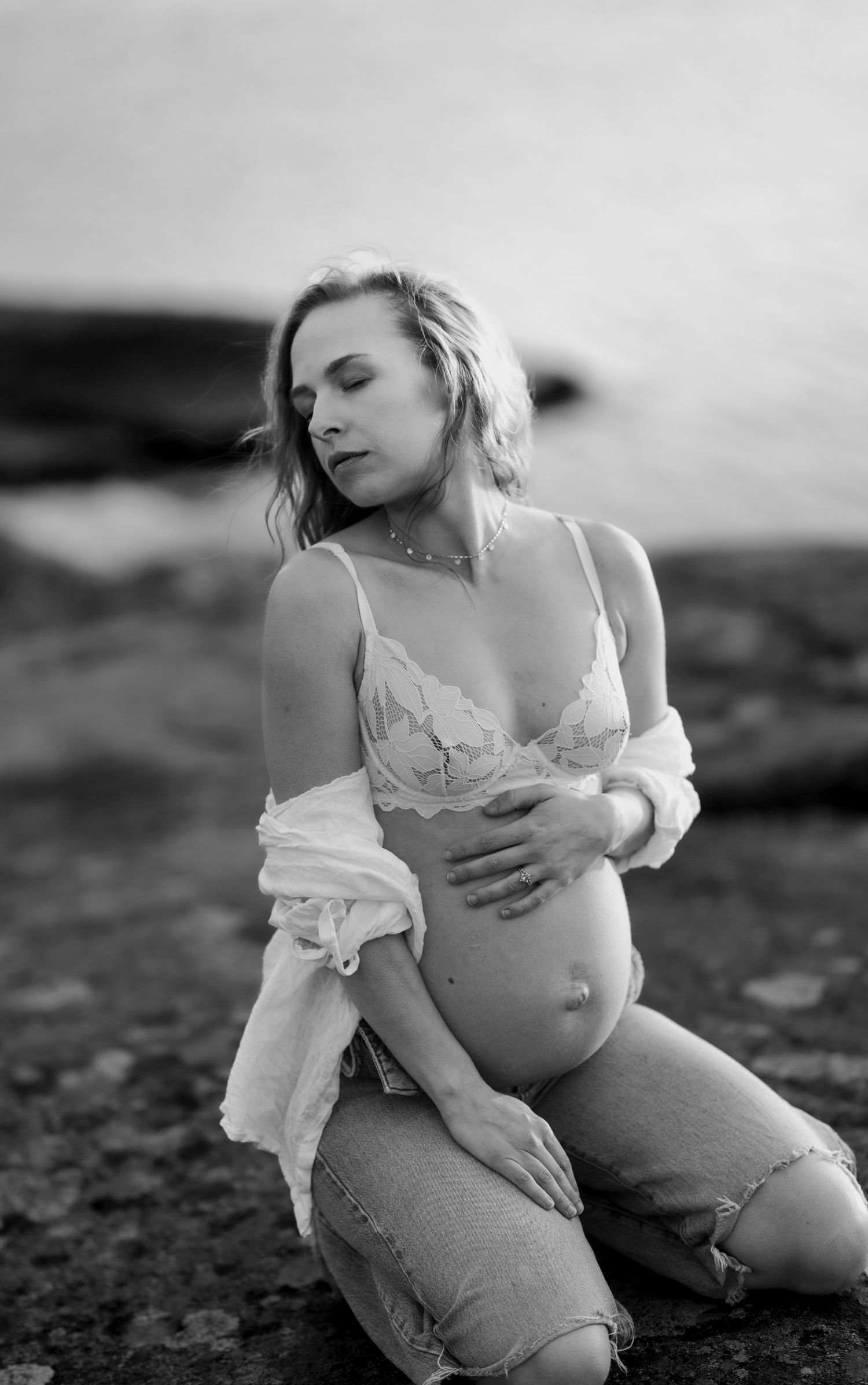 gravid kvinna sitter på knä på en klippa. hon håller sig om magen och kollar bortåt.