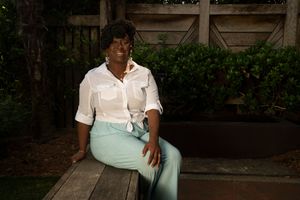A person wearing a white shirt and mint green pants sits casually on an outdoor bench.