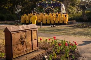 A wooden memorial plaque near red tulips with a group wearing yellow jackets gathered in the background.