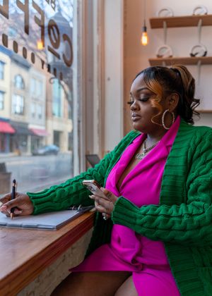 A person in a bright pink shirt and green cardigan sits by a window in a contemplative sequence of poses.