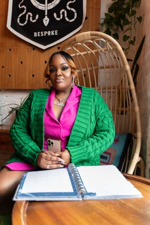 Professional working at wooden desk wearing vibrant green quilted jacket and pink top while reviewing documents.
