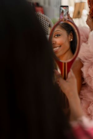 Reflection in mirror shows bright smile and festive pink attire in warm lighting.