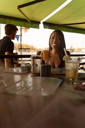 People enjoying drinks at an outdoor bar with a green umbrella canopy overhead during a sunny day.