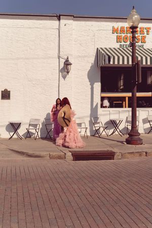 A sequence of photos showing pink and red dresses moving across a brick boardwalk near a market house.