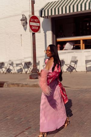 A person in a flowing pink dress twirls gracefully in front of a brick wall with folding chairs in the background.