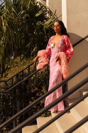 Fashion sequence showing pink dresses and feather details on outdoor stairs with foliage.