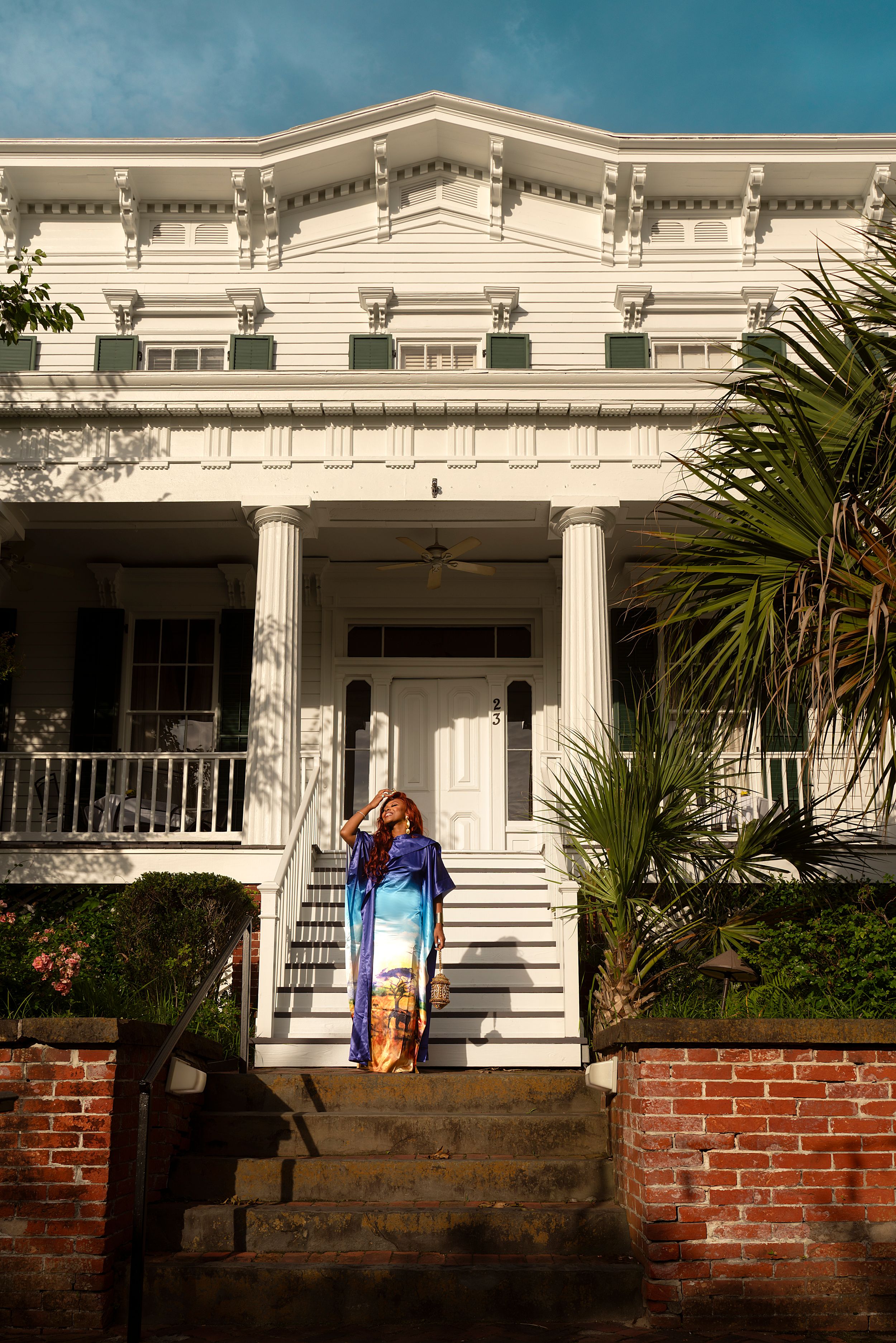A series of white colonial-style house facades with brick foundations and palm trees in the foreground.