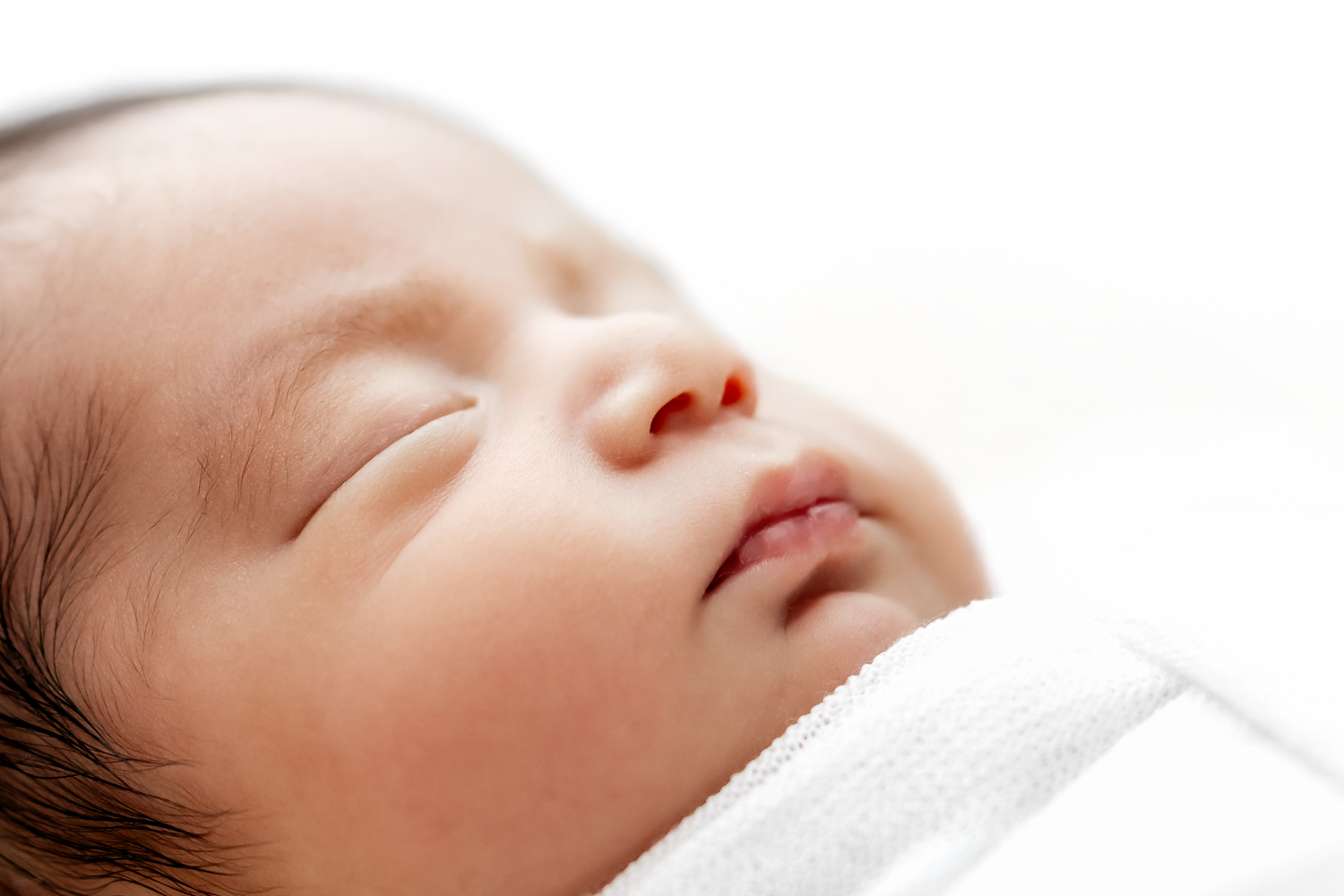 A peaceful newborn baby sleeps soundly wrapped in a soft white blanket.