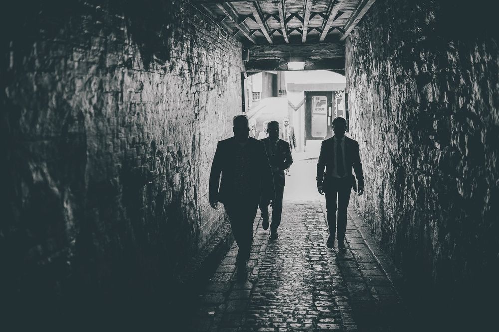 Silhouettes of people walking through a dark tunnel with bright light at the end creating a moody atmosphere.