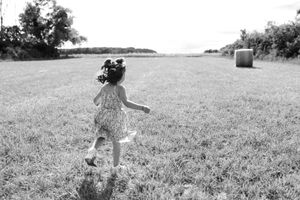 Photo en noir et blanc d'une petite fille qui court pendant une soirée ensoleillée dans les champs de blés