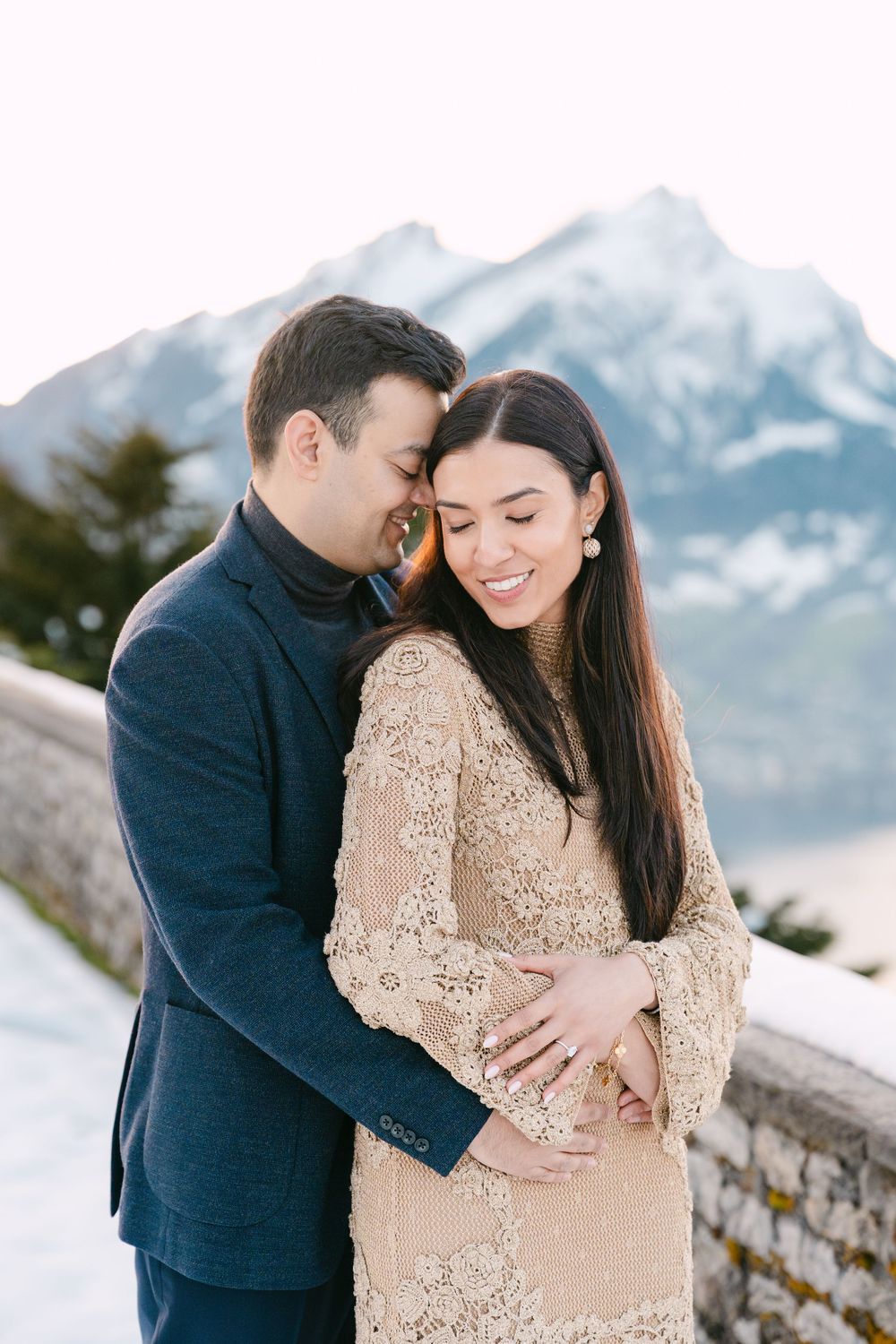 A romantic couple embraces in the snow with majestic mountain peaks in the background.