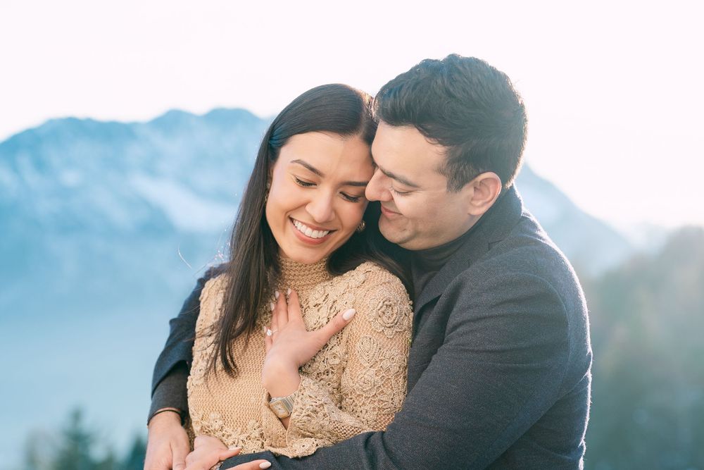 A couple shares an intimate moment while embracing outdoors against a scenic mountain backdrop.