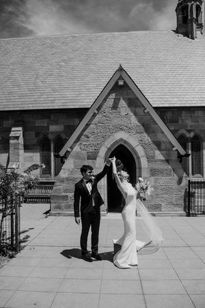 Black and white wedding sequence showing couple dancing and twirling on stone courtyard in front of church building.