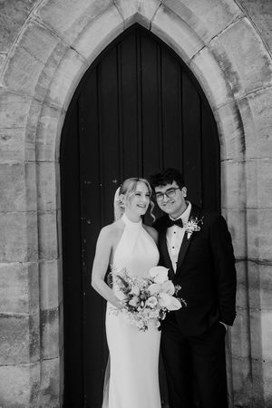 A romantic black and white wedding photo series showing a couple in traditional attire standing beneath stone church archways.
