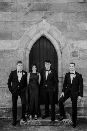 Black and white photo of a formal wedding party standing in front of a gothic stone church doorway.