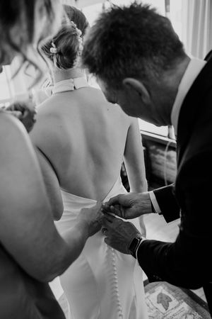 A series of black and white wedding photos showing intimate moments as a bride gets help with her dress buttons.