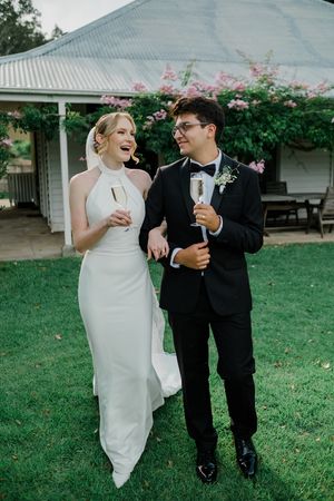 A couple in wedding attire share a joyful moment while walking together on a green lawn.