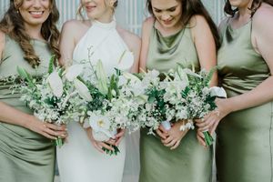 Bridesmaids in sage green dresses hold white and green floral bouquets during an elegant outdoor wedding ceremony.