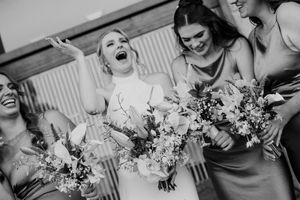 Black and white photo of bridesmaids in matching dresses sharing a joyful moment with bouquets.