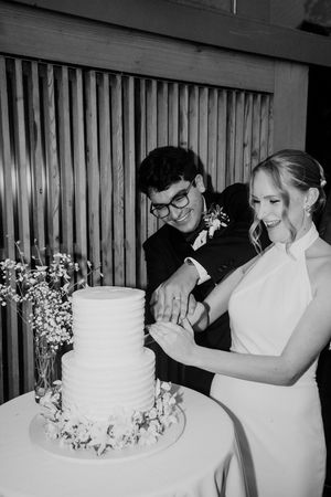 A series of black and white photos showing a couple cutting their white tiered wedding cake together.