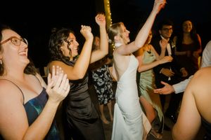 People dancing and celebrating at a lively party or wedding reception with raised arms and joyful expressions.