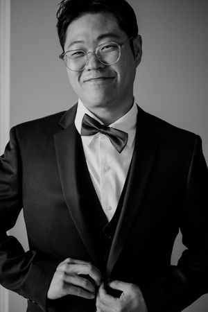 Black and white portrait of a person in formal attire wearing glasses, a bow tie and three-piece suit.