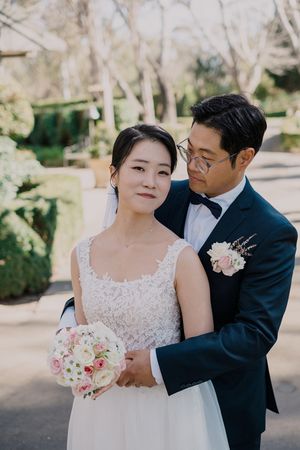 Bride in white lace gown and groom in navy suit share intimate moments during outdoor wedding photo session.