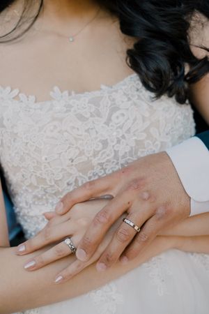 Close-up view of hands wearing white lace and an engagement ring showing off wedding day details.