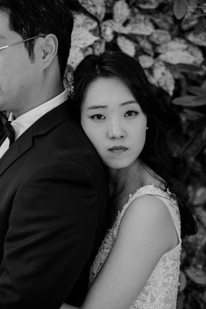 A black and white artistic wedding photo showing a couple posing back-to-back in formal attire.
