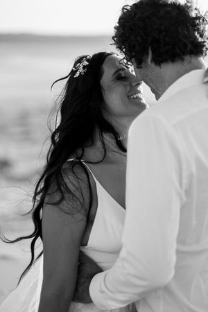 Black and white romantic beach photo series showing a couple embracing with wind-blown hair and white attire.