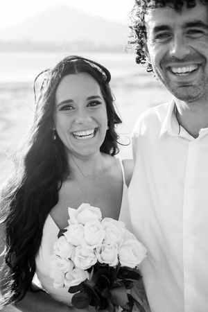 A happy couple in black and white poses together on their wedding day holding white roses.