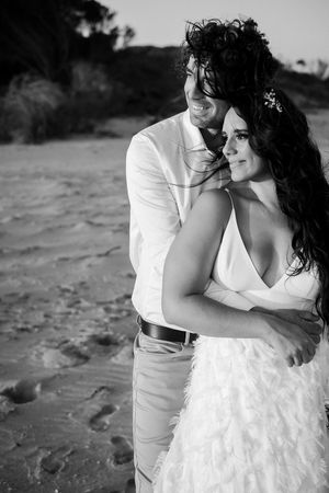 A romantic black and white portrait of newlyweds embracing outdoors in formal wedding attire.