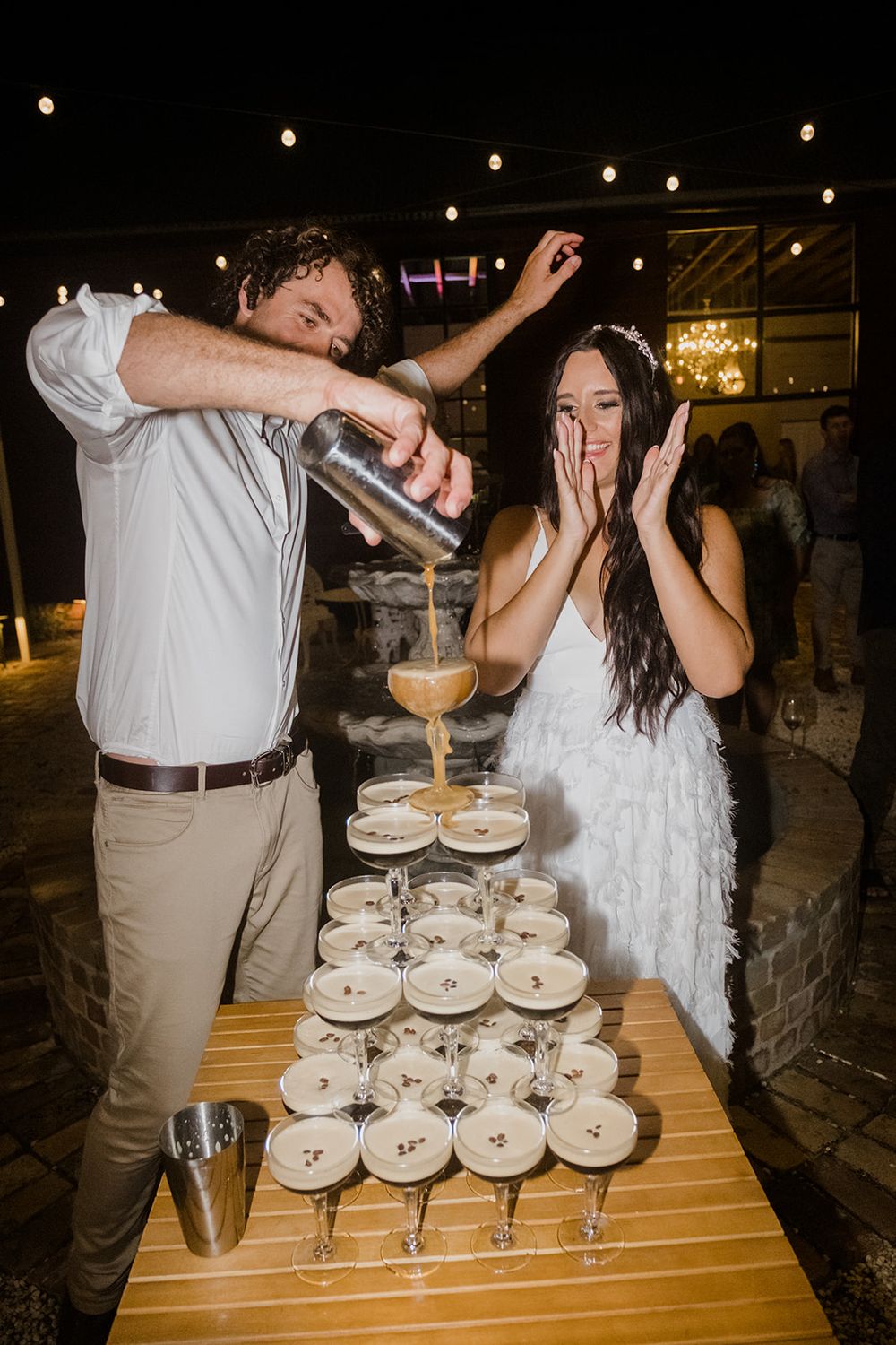 Wedding couple pours champagne into a tower of glasses at their reception celebration.