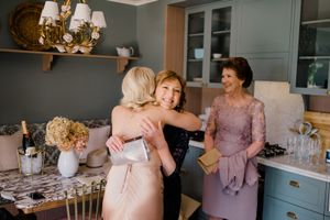 Wedding party in pastel pink and purple dresses gather around an elegant table setting at an indoor reception.