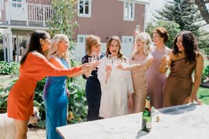 A group of women in colorful dresses toast with champagne glasses during a celebratory outdoor gathering.