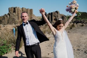 A couple celebrates their wedding day with joyful poses against a scenic rocky coastal backdrop.