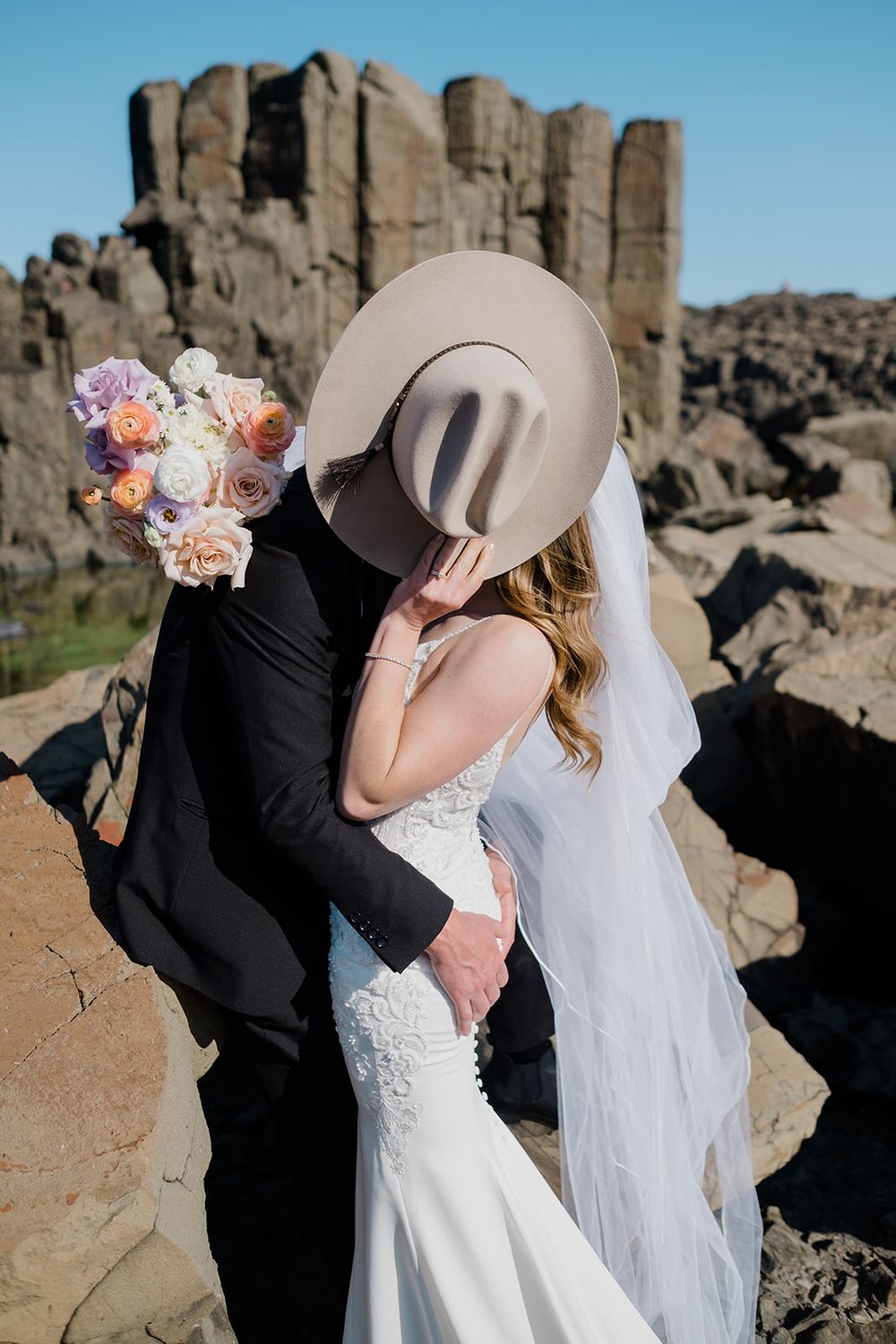 A romantic wedding couple shares intimate moments against dramatic rock formations at sunset.