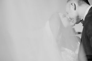 A romantic black and white wedding photograph showing a tender moment through a soft veil.