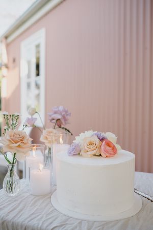 Elegant white wedding cake decorated with peach and blush roses on a white tablecloth with glowing candles.