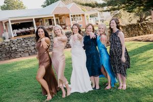Wedding party poses together on a sunny lawn outside a stone building during an outdoor celebration.