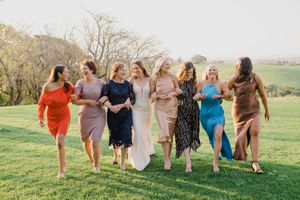 A group of friends in colorful dresses walking together through a grassy field at sunset.