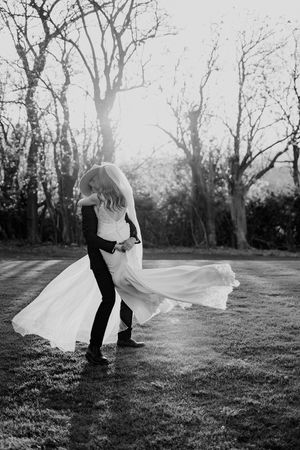 Black and white photo series showing a flowing wedding dress moving gracefully in the wind on a grassy field.