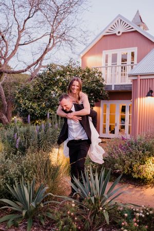 A romantic photo series at dusk shows a couple embracing in front of a pink cottage with desert landscaping and agave plants.