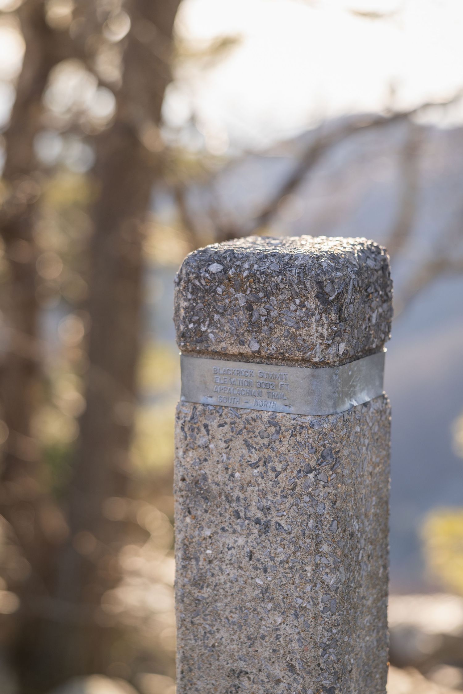 Close-up view of a weathered concrete post with rough textured surface against a blurred natural background.