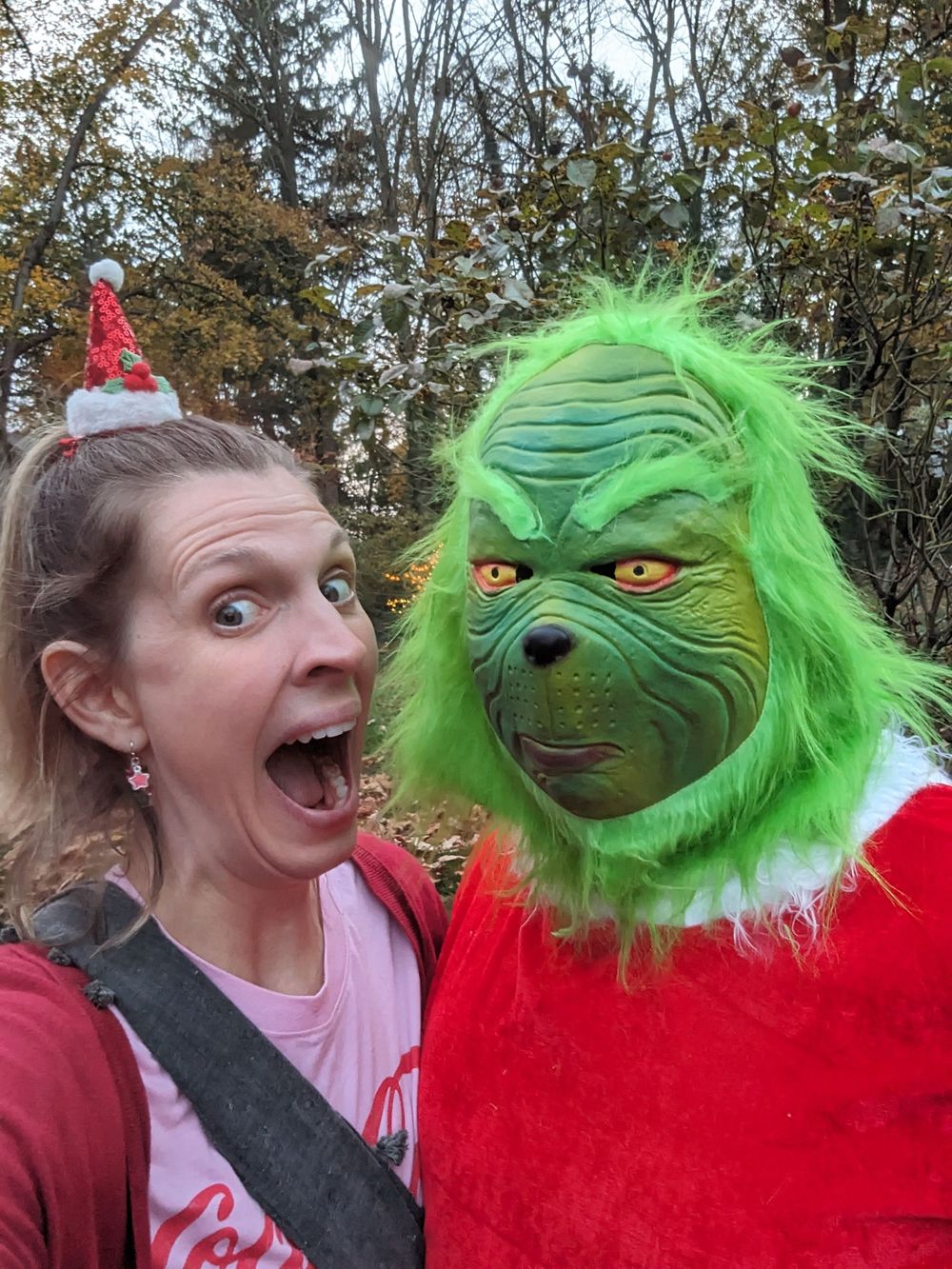 A selfie with someone posing next to a person in a green Grinch costume wearing a red Santa suit.